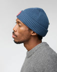Man wearing a blue knit beanie and gray sweater against a plain background