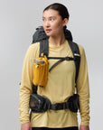 Person wearing a yellow long-sleeve shirt with a black backpack and yellow hydration pack on a gray background