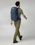 Person carrying a blue hiking backpack on a plain background