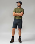 Man wearing a green t-shirt, black shorts, and a cap on a gray background
