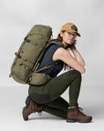 woman waring navy top and green tights with reinforced knees and brown cap, carrying a trekking backpack