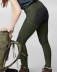woman wearing green tights with reinforced knees holding up a trekking backpack