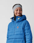 Person wearing a blue puffer jacket with a visible Fjällräven logo on a plain background