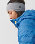 Person wearing a blue puffer jacket and gray headband on a light gray background