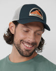 Man wearing a cap with a visible Fjällräven logo on a plain background