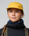Person wearing a yellow cap and dark jacket with a backpack on a gray background