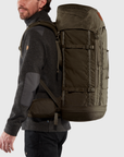 Man wearing a large green hiking backpack on a light gray background