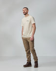 Man wearing a beige t-shirt, brown pants, and brown boots on a gray background