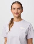 Woman wearing a light purple t-shirt with a fjallraven logo on a white background
