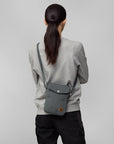 Person wearing a gray crossbody bag on a plain background