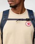 Person wearing a navy backpack with a visible Fjällräven logo on a plain background
