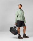 Person wearing a light green jacket and black shorts, holding a black bag on a gray background