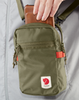 placing phone inside a green small sling bag with Fjällräven logo