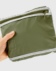 Green travel pouch with a zipper held by a hand on a light gray background