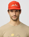 Man wearing a red cap and beige t-shirt with a logo on a light gray background