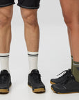 Two pairs of legs wearing different socks and shoes on a plain background