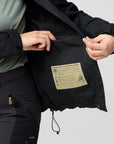 Person adjusting a black jacket with a patch on a gray background