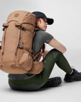 Person sitting with a large brown backpack on a light gray background