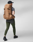 Person wearing a large brown backpack on a light gray background