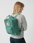 Person wearing a green backpack with a visible Fjällräven logo on a plain background
