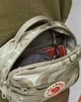 Small backpack with a visible Kanken logo, filled with items, against a neutral background.