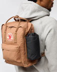 Person wearing a brown backpack with a visible Fjällräven logo on a plain background