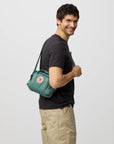Man holding a green bag with a visible brand logo on a light gray background