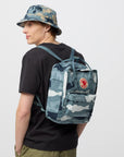 Person wearing a camouflage backpack and hat on a white background