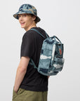 Person wearing a camouflage backpack and hat on a plain background