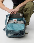 Person opening a blue camouflage backpack on a white background