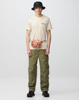 Person wearing a beige t-shirt, green pants, and a black hat on a white background