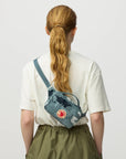 Person wearing a blue Fjällräven bag over one shoulder on a plain background