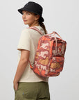 Person wearing a red camouflage backpack with a visible brand logo on a light gray background