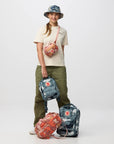 Person holding a camouflage backpack with two additional bags on a white background