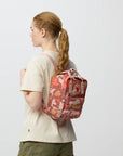 Person wearing a red camouflage backpack on a plain background