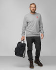 man in grey sweater and black trousers carrying black Kanken backpack