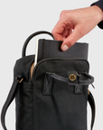 slipping a notebook into a black sling bag with handle