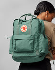 Person wearing a green backpack with a visible Fjällräven logo on a gray background