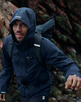 man in navy windbreaker jacket with hood trekking in mountain