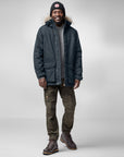 man wearing dark navy parka with fur hood and grey trekking trousers and black beanie