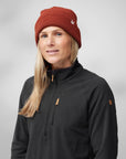 Woman wearing a black fleece jacket and red beanie with a logo on a gray background