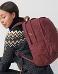 Woman wearing a maroon backpack on a plain background