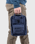 Person holding a navy blue backpack with a visible Fjällräven logo on a light gray background