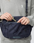 Person opening a navy blue Fjällräven bag with a key against a light gray background