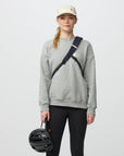 Person wearing a gray sweatshirt and black pants, holding a helmet, on a light gray background