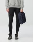 Person wearing black leggings with a logo, holding a navy backpack on a light gray background