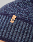 Close-up of a blue knit beanie with a leather tag on a gray background