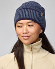 Person wearing a blue knit beanie and beige jacket on a gray background