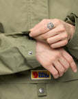 Person wearing a green jacket with Fjällräven logo, adjusting the jacket's button.