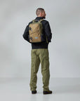 Person wearing a tan and green backpack on a plain background